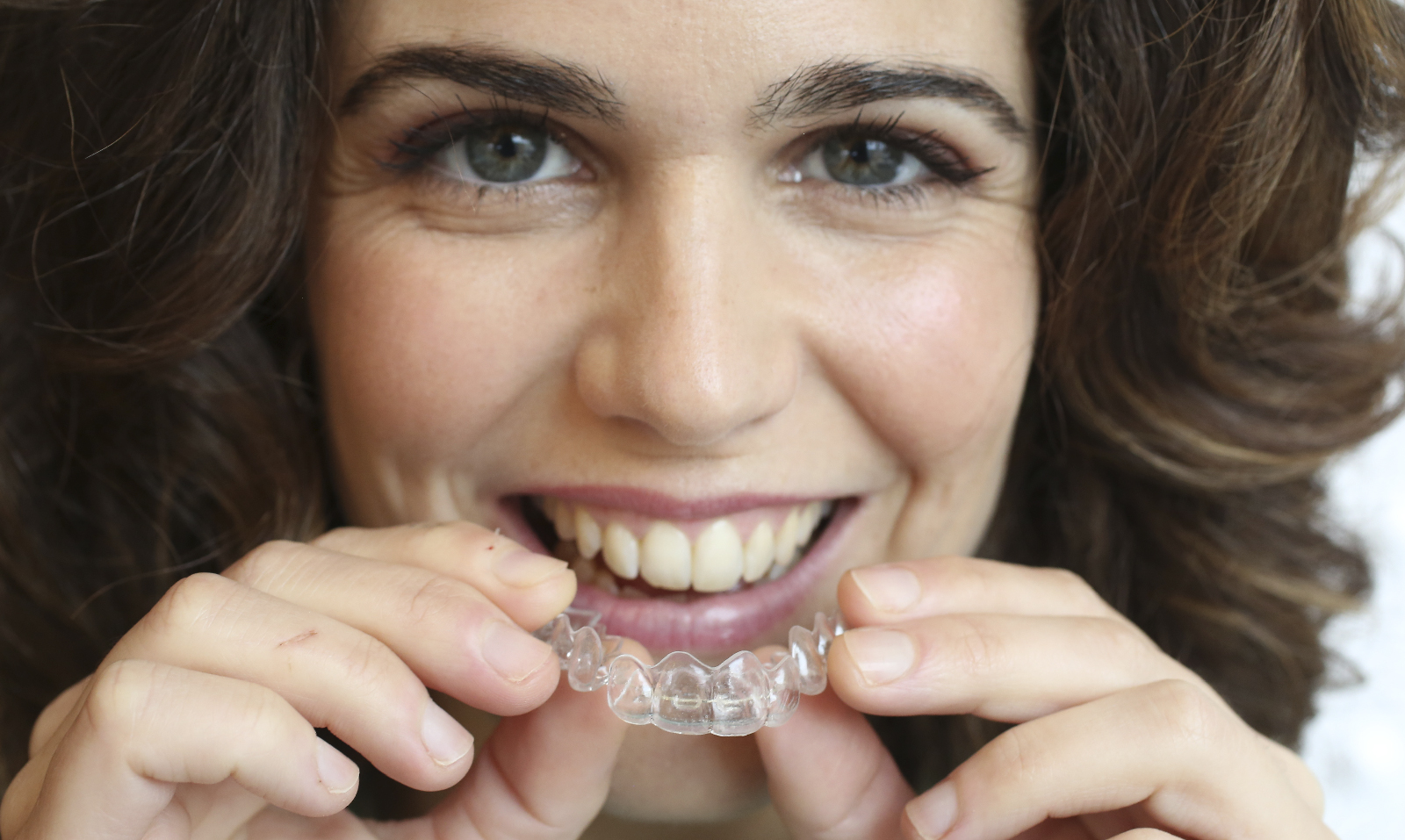 Mujer sonriendo con alineador transparente en la mano