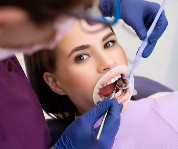Dentist uses dental tools and mirror to check the teeth of woman patient